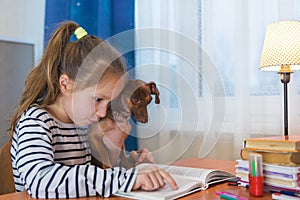 Child with dog reading book at home. Girl with pet sitting at window at read