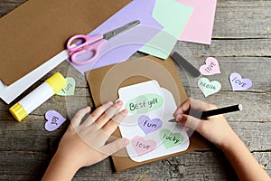 Child doing a birthday card. Child holds a black marker in hand and writes. Paper greeting card with jar, hearts and wishes