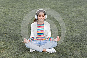 Child doing exercise on green grass. Healthy lifestyle and relax. Yoga girl. small kid wear headset. meditation summer