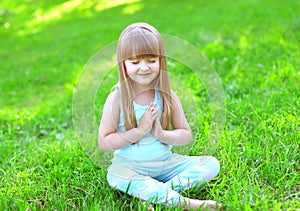 Child doing yoga exercises sitting on the grass