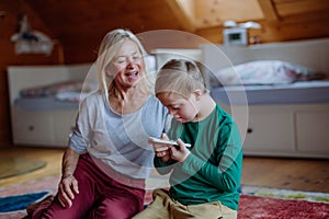 Child with Down syndrome sitting on floor and using tablet with grandmother at home.