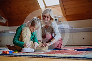 Child with Down syndrome sitting on floor and using tablet with grandmother at home.