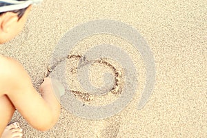 Child draw heart on sand
