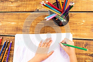 Child drawing with colorful pends on wooden desk