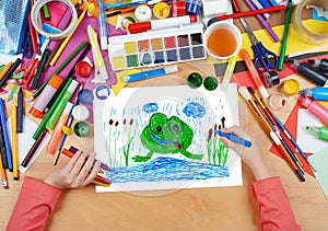 Child drawing frog in river, top view hands with pencil painting picture on paper, artwork workplace