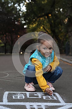 Child drawing house with chalk on asphalt