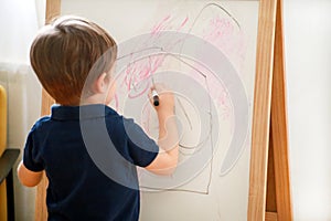 Child is drawing and painting with felt pen on paper of wooden drawing board artist easel for kids and children at home. Childhood