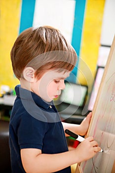 Child is drawing and painting with felt pen on paper of wooden drawing board artist easel for kids and children at home. Childhood