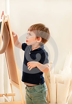 Child is drawing and painting with felt pen on paper of wooden drawing board artist easel for kids and children at home. Childhood