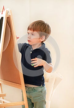 Child is drawing and painting with felt pen on paper of wooden drawing board artist easel for kids and children at home. Childhood