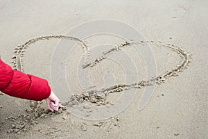 Child is drawing in the sand a heart.