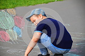 Child drawing sun and house on asphalt in a park on the playground or sidewalk, happy childhood, summer vacation