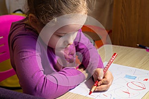 The child draws. The girl is sitting at the table. Colour pencils. Applications. Children`s handwork.