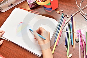 The child draws a heart on paper with colored pencils at home at the table