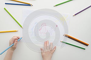 A child draws his family with pencils. Child`s drawing and colored pencils. Family drawing on a white paper. Top view