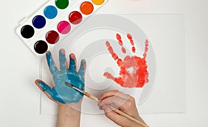 The child draws his hand with blue paint and a brush. Finger painting or art therapy for children