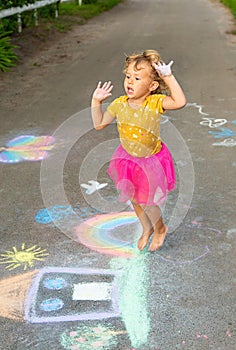 A child draws a house and a rainbow on the asphalt with chalk. Selective focus.