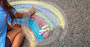 A child draws a rainbow on the asphalt. Selective focus.