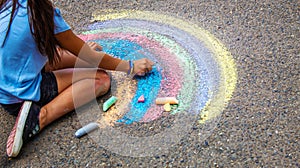 A child draws a rainbow on the asphalt. Selective focus.