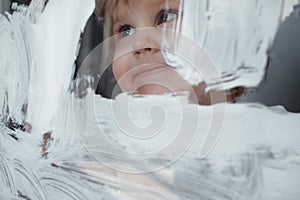 The child draws a white paint on a glass Board. Simulated screen. Happy child with brush