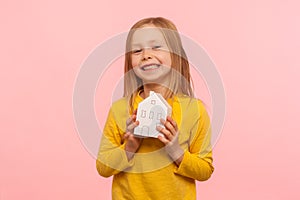 Child dreaming of home. Portrait of happy cute little girl holding paper house and smiling to camera