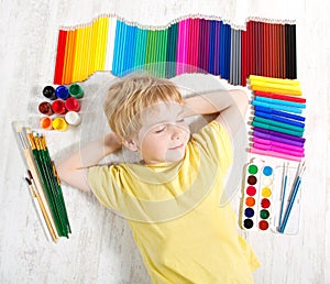 Child dreaming next to pencils, brushes, paints