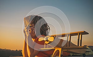 Child dreams and imagination concept. Dreaming child playing with toy wooden airplane against summer sky background