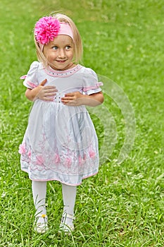 Child in a dress and with a red bow and a sly look on a background of green grass