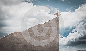 Child dressed as an aviator with cardboard plane at the top of very high stairs photo