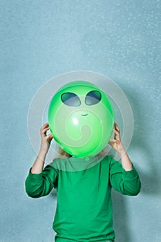 Child dressed in green clothes playing alien. girl with a green ball where eyes and faces are drawn