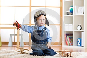 Child dressed like pilot aviator plays with a toy airplanes at home in his room