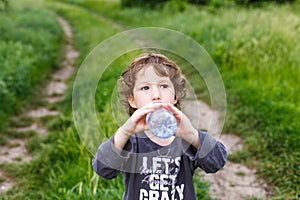 Child drinking pure water in nature. Cute curly toddler