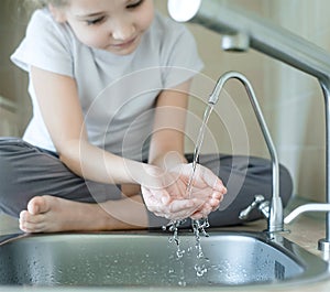 Child drinking water in kitchen at home. Thirsty baby. Hands open for drinking tap water. Pouring fresh drink. Water quality check
