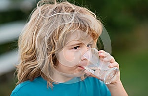 Child drinking water outdoor in park. Kid drinking. Close up portrait of boy drink water from glass in the garden.