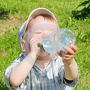 A child drinks water from a bottle. The child, the boy, quenches