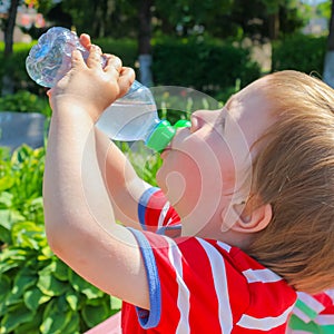 A child drinks water from a bottle. The child, the boy, quenches