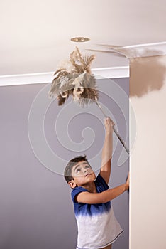 Child, dusting and ceiling in house for spring cleaning, learning responsibility and development. Young boy, kid or