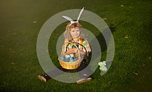 Child with easter eggs in basket outdoor. Boy on grass in park. Easter egg hunt. Fynny kids portrait. Cute bunny child