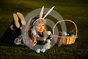 Child with easter eggs in basket outdoor. Boy laying on grass in park. Easter egg hunt. Fynny kids portrait. Child bunny