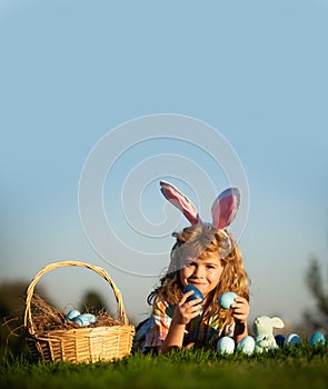 Child with easter eggs in basket outdoor. Boy laying on grass in park, on sky background with copy space. Easter egg