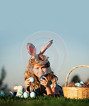 Child with easter eggs in basket outdoor. Boy laying on grass in park, on sky background with copy space. Easter egg