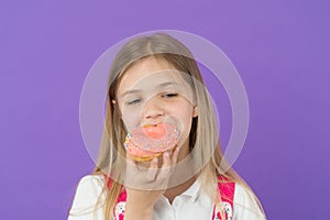 Child eat donut on violet background. Little girl bite glazed ring doughnut. Candyshop concept. Childhood and happiness