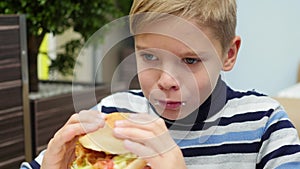 Child eating a bun with chicken, cheese and greens in a fast food restaurant