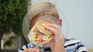 Child eating a bun with chicken, cheese and greens in a fast food restaurant