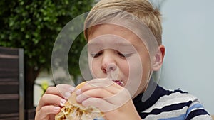 Child eating a bun with chicken, cheese and greens in a fast food restaurant