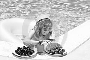 Child eating fruits near swimming pool during summer holidays. Kids eat fruit outdoors. Healthy fruits for children.