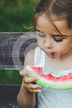 Child eating watermelon in the garden. Kids eat fruit outdoors. Healthy snack for children. Beautiful background, emotion girl