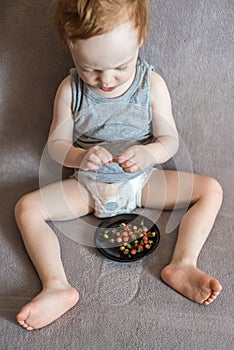 Child eating wild strawberries at home on the sofa.  Cute toddler boy