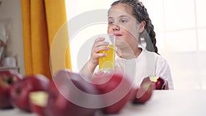 The child eats an apple and drinks juice. Healthy eating fruit concept. Child brunette girl eating an apple on the table