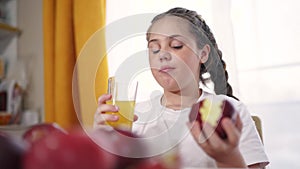 The child eats an apple and drinks juice. Healthy eating fruit concept. Child brunette girl eating an apple on the table